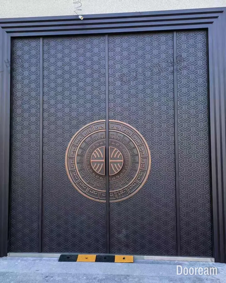 Bronze-finish four-leaf entrance door with a geometric relief and a fret-pattern medallion, installed at a client's home